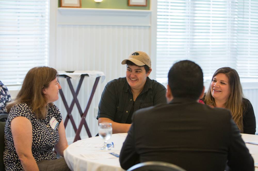 Faculty members talk and laugh at a table.